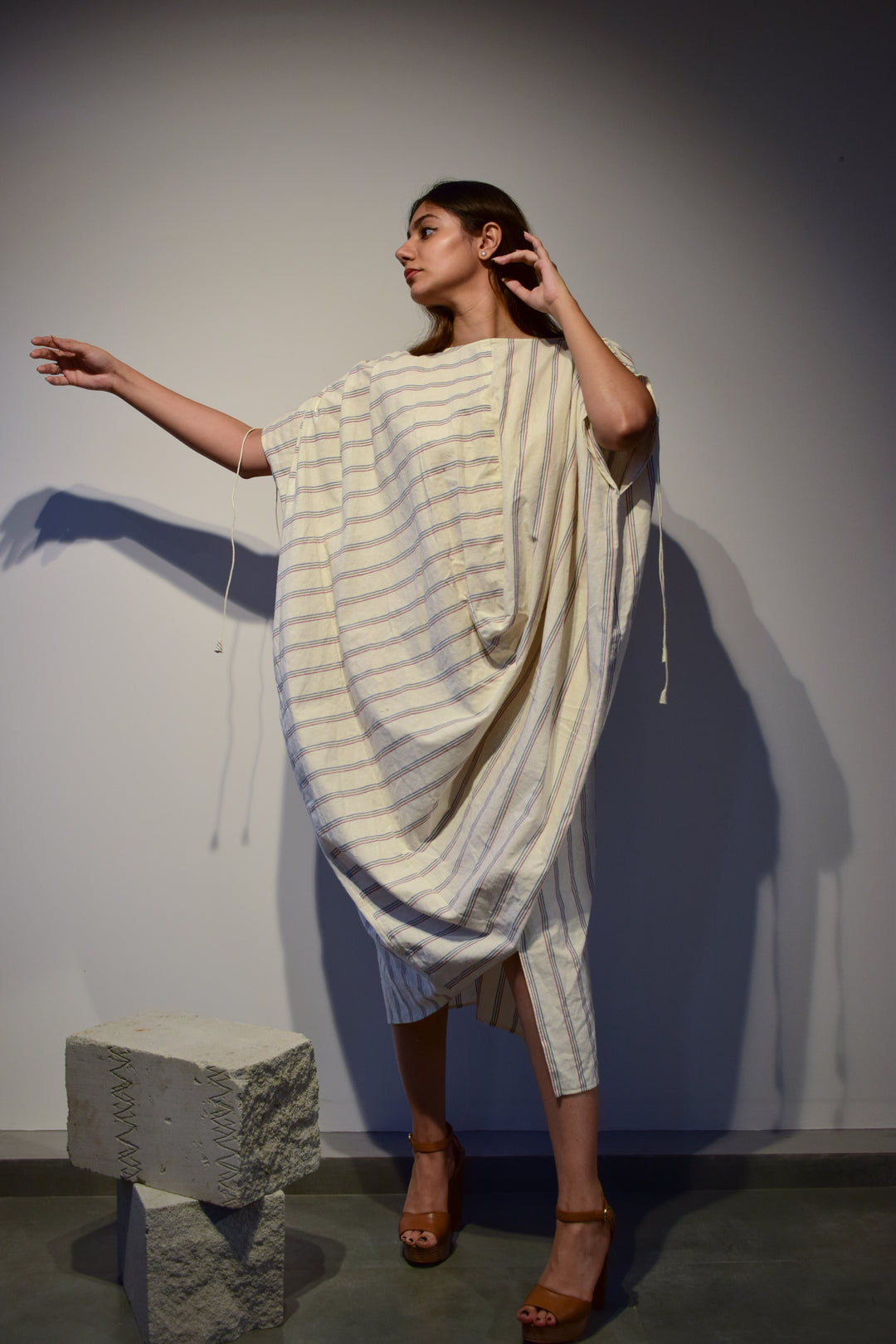 A white tunic dress with stripe pattern within the textile. It features drawstring sleeves