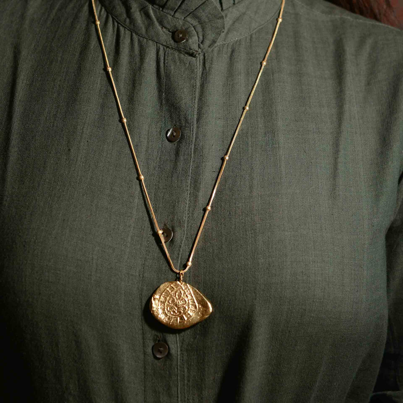 A dye gold pendant on a chain, which is made to resemble a fossil.