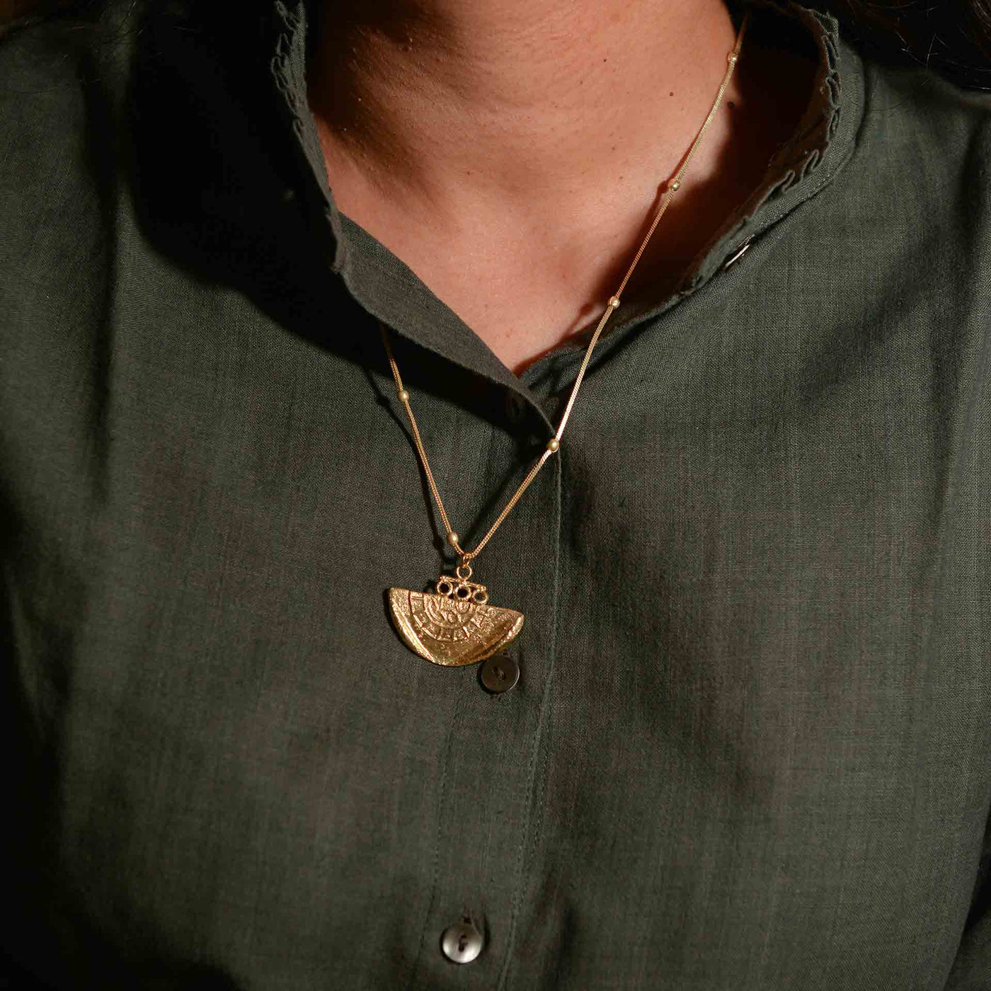 A dye gold pendant on a chain, which is made to resemble a fossil.