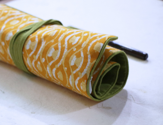 Yellow Block Print Roll-up case tied using a Green cord that has a tassel attached to it.